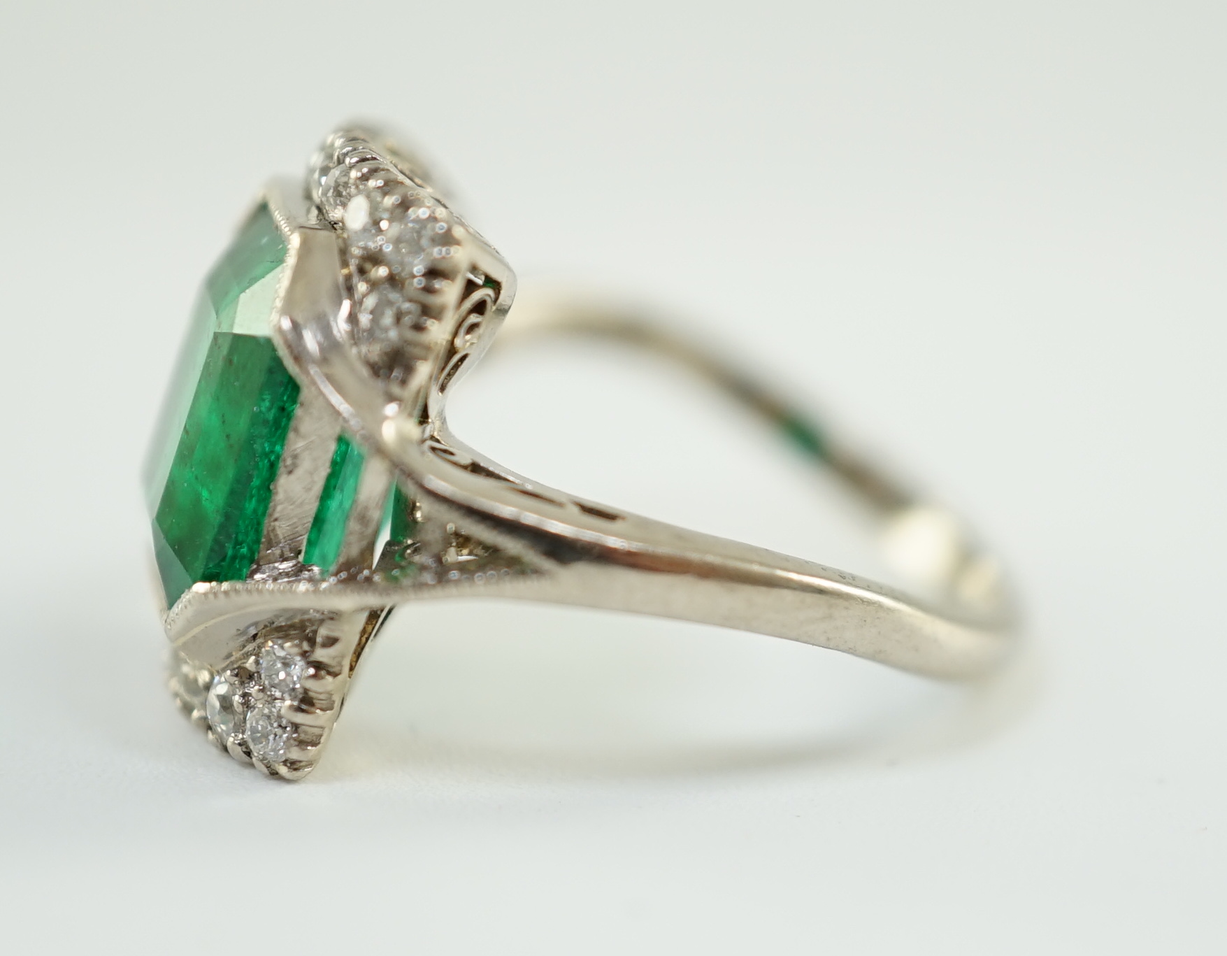 An Art Deco 18k white gold, emerald and diamond set square cluster dress ring, with shaped cut sapphire set shoulders, (a.f.)